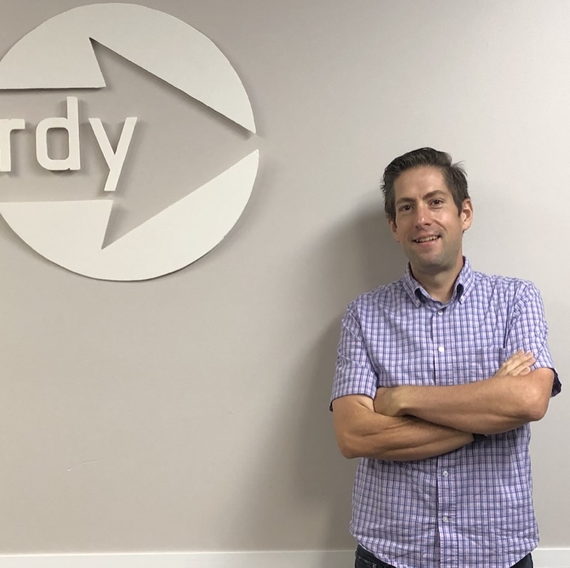 Kevin Young smiling with his arms crossed in front of the RdyToGo logo on an office wall