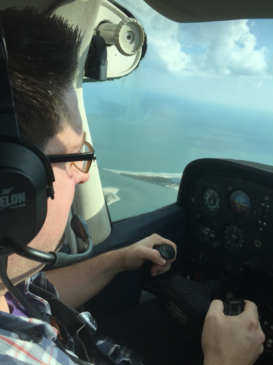 Kevin Young usando um fone de ouvido e segurando o manche da Cessna, com Murrells Inlet visível pela janela.